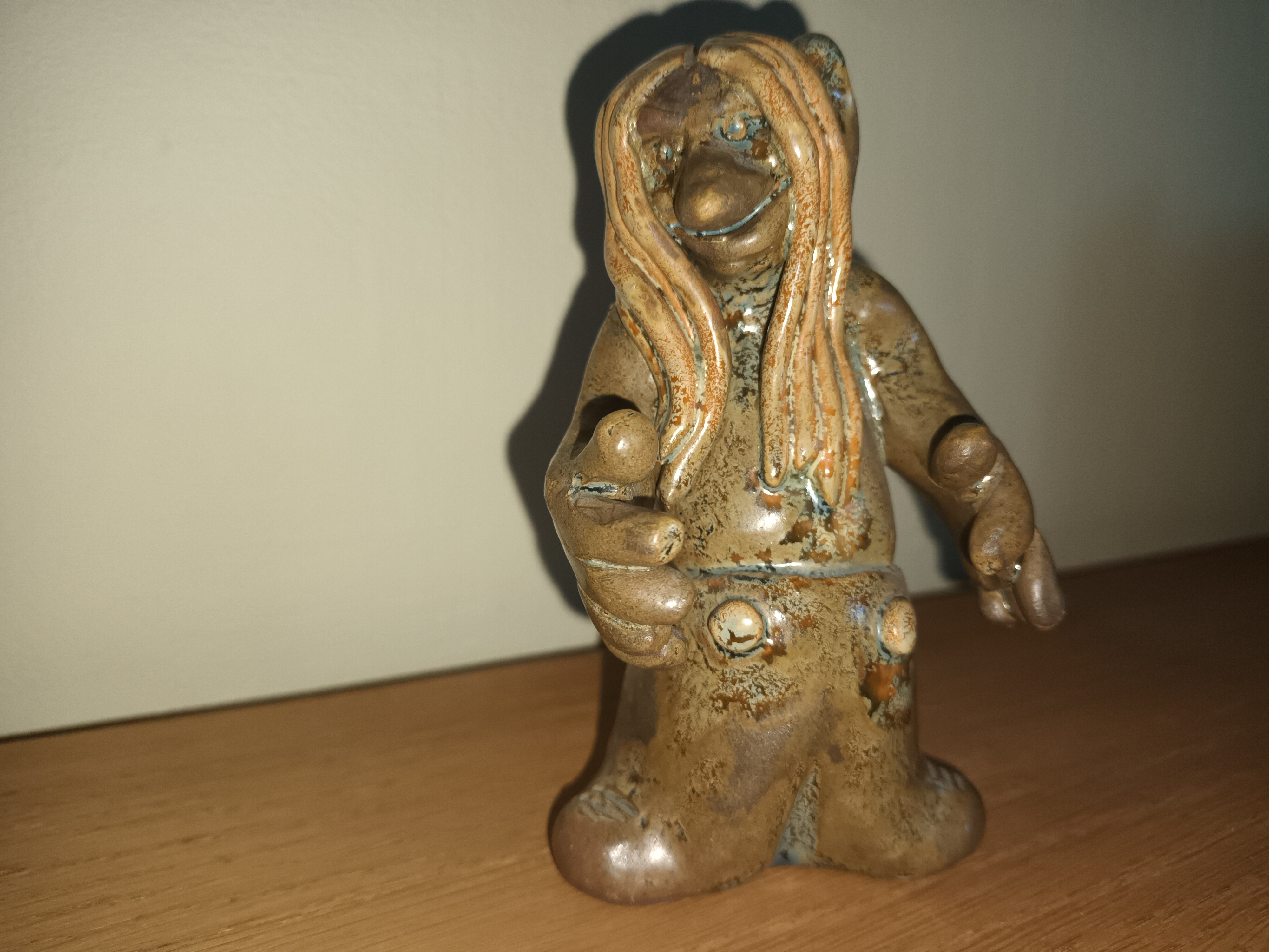 Keramikfigur av ett troll med stora händer och långt hår, handgjord av Tore Borg